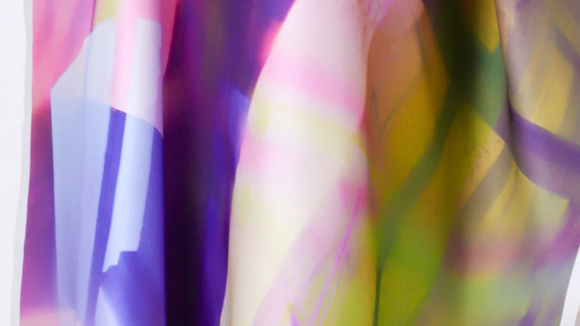 Close-up of a translucent, hanging textile installation. The fabric is draped in soft folds, featuring a dreamlike wash of ethereal colours including violet, soft pink, pale yellow, and lime green, resembling a blurred, light-filled landscape.