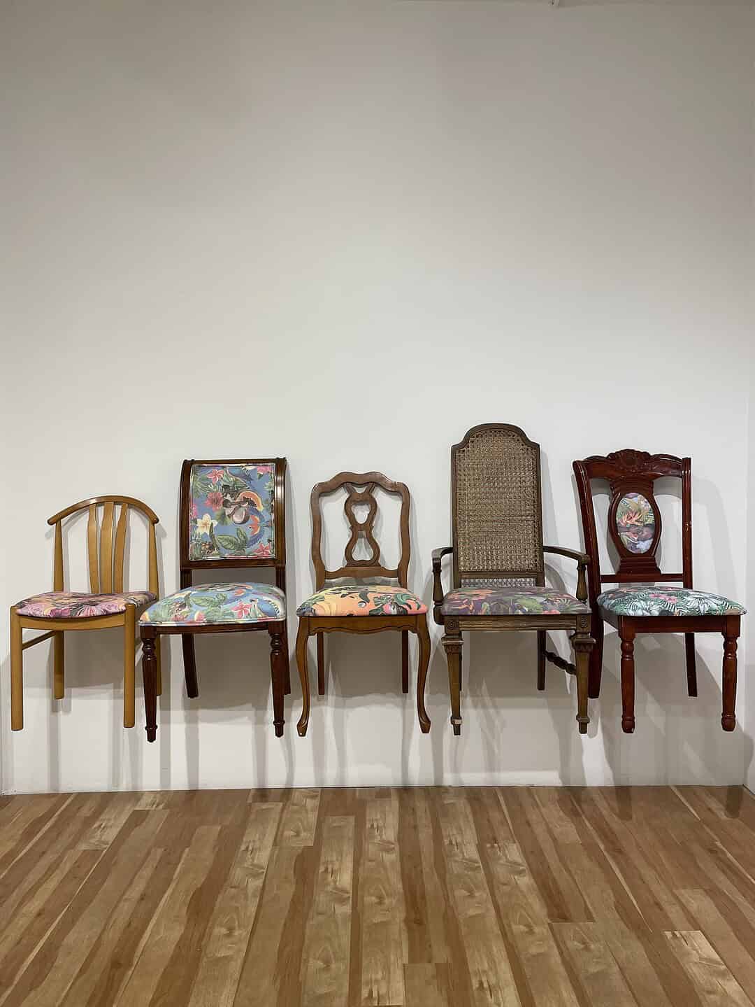 Row of five vintage wooden chairs with seats upholstered in colourful tropical patterned fabric against a gallery wall