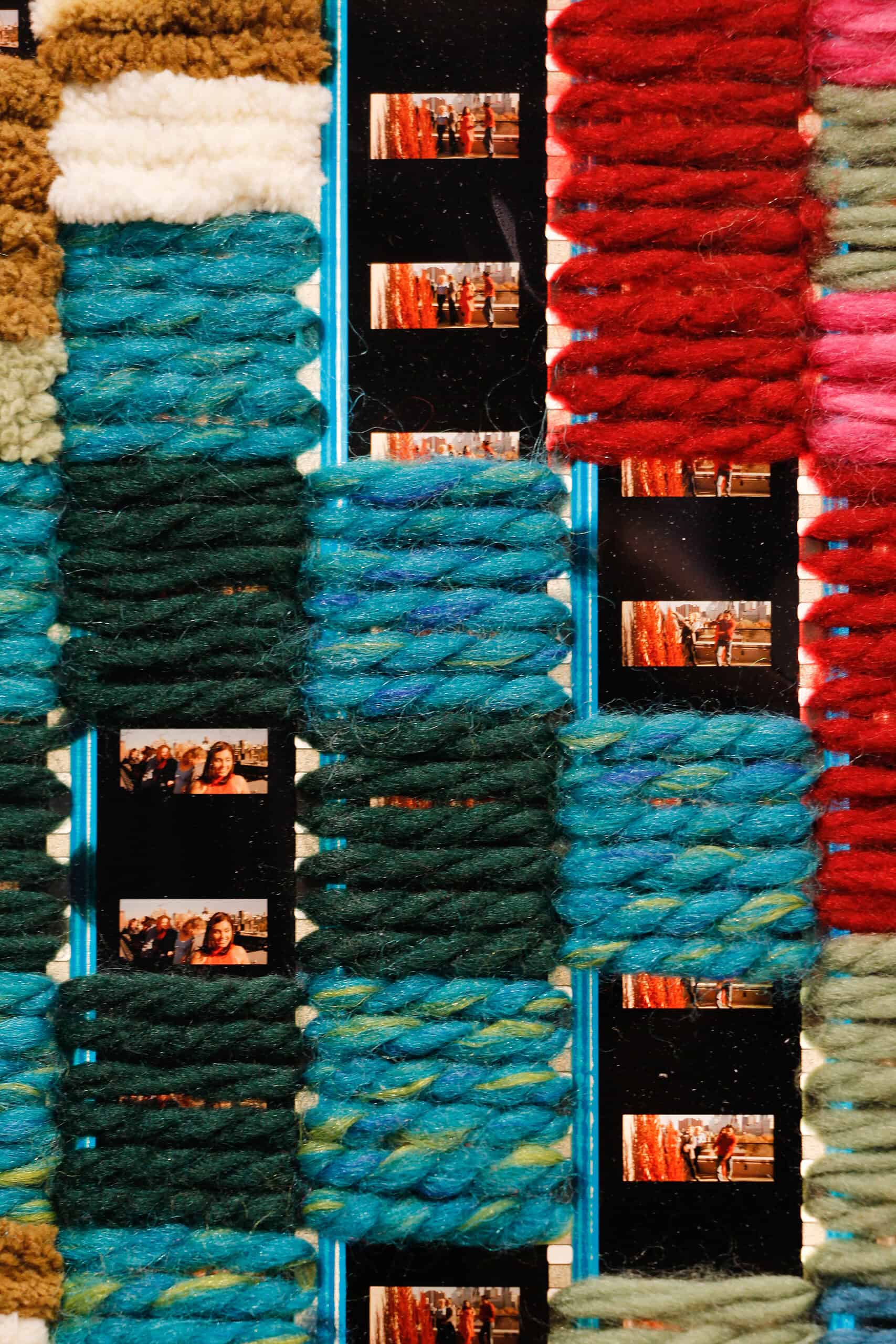 Close-up of woven yarn in teal, blue, and red tones interlaced with vertical strips of photographic film
