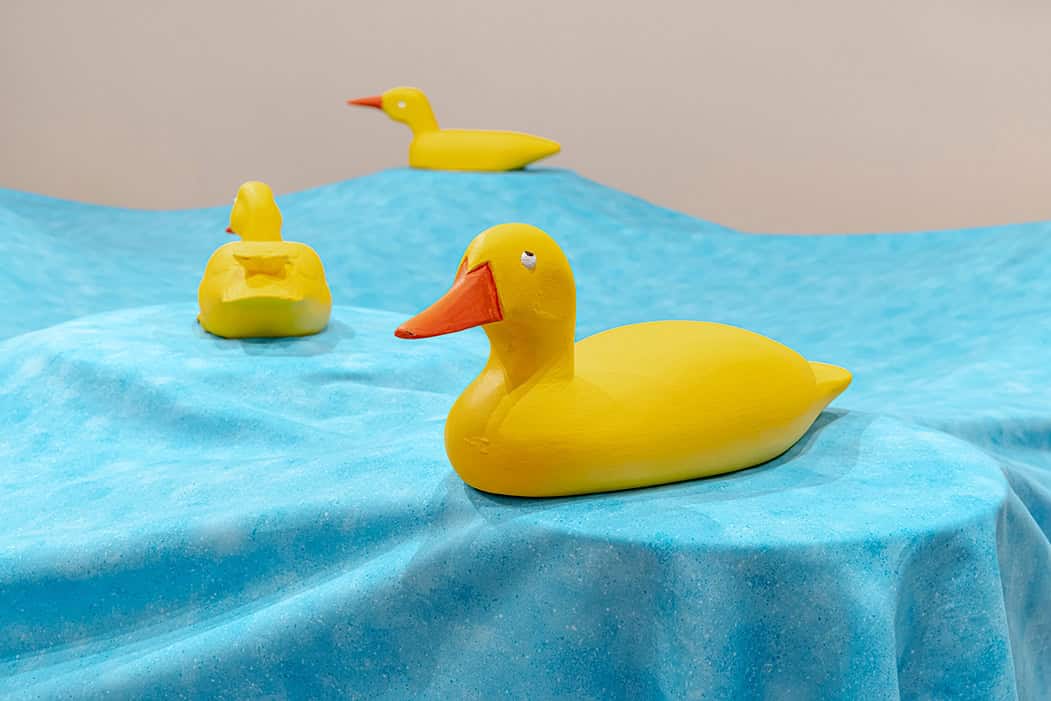 Three small yellow duck sculptures placed on a textured blue surface resembling water