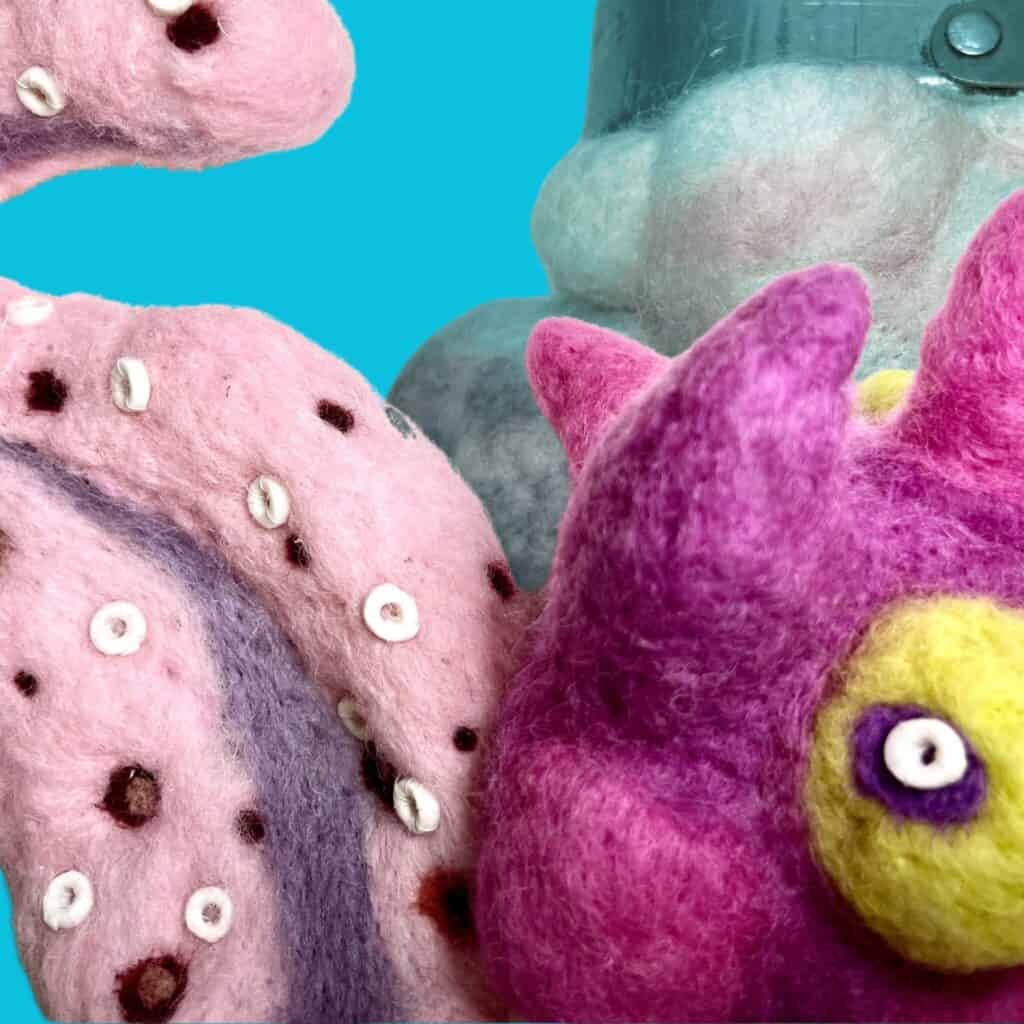 Close-up of brightly coloured felted sculptures with pink, purple, and yellow textures and round white details, set against a solid teal blue background.