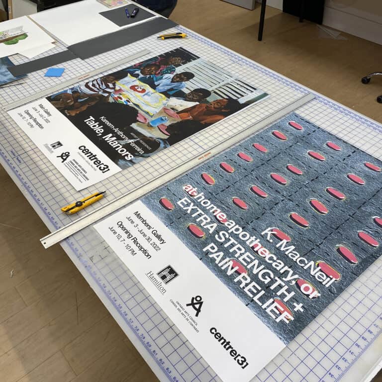 Two large-format posters on a grid-lined cutting table in the Digital Printing Studio.