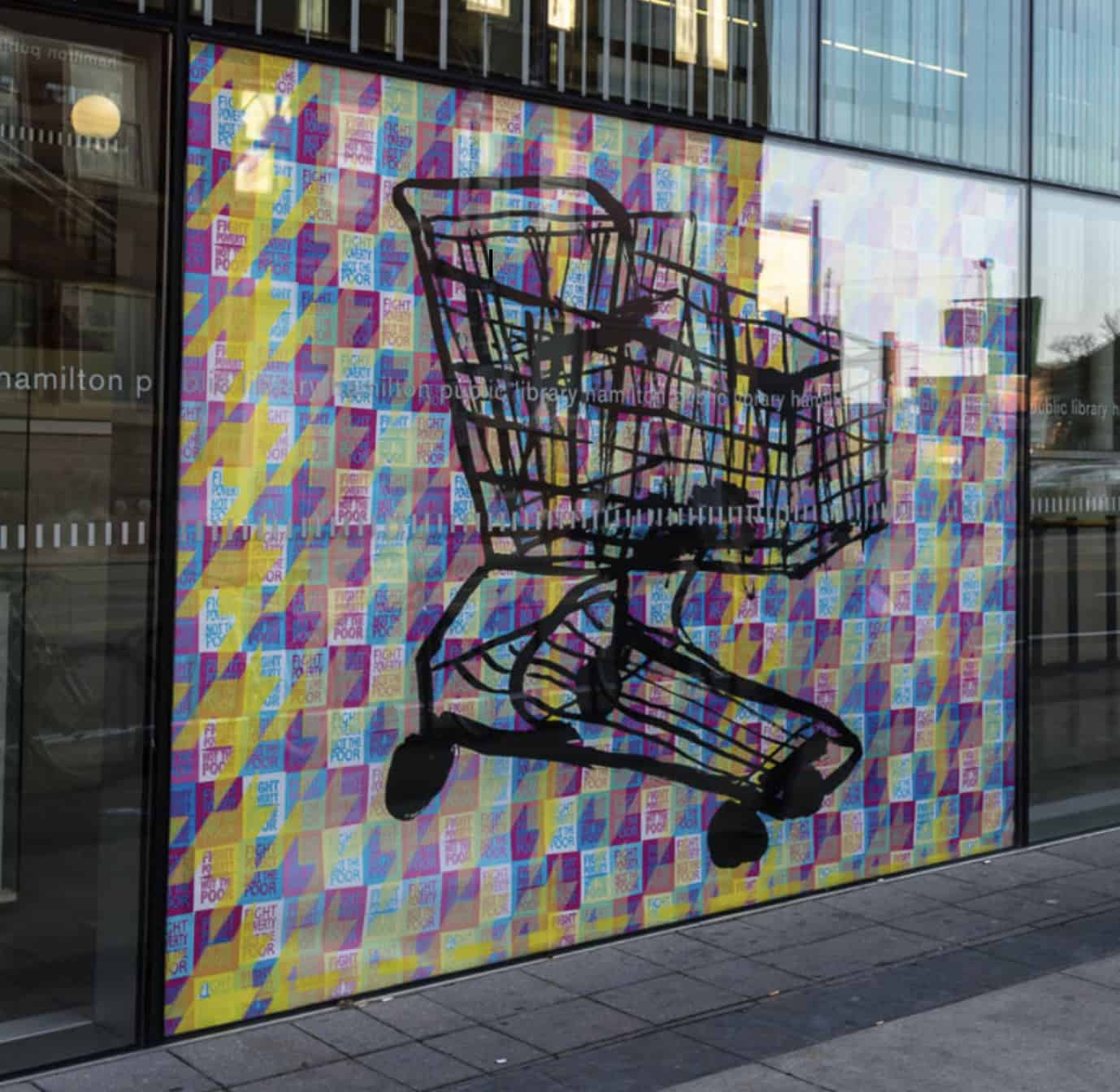 A large black shopping-cart outline painted over a glass wall covered in a pastel geometric pattern of poster prints.