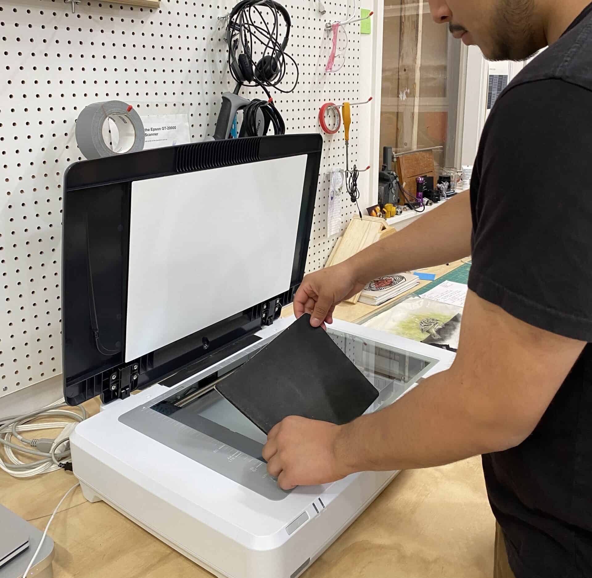 A person placing artwork on the glass of an Epson flatbed scanner in the Digital Printing Studio.