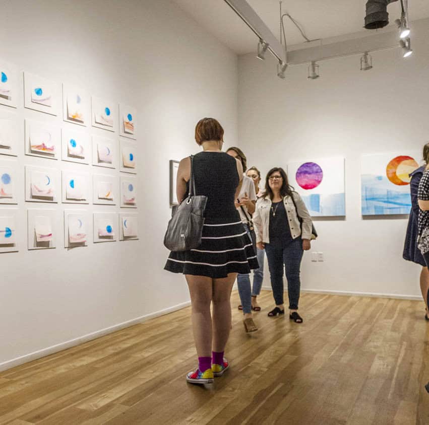 People viewing abstract art in the Centre[4]Arts gallery, with white walls and wooden floors.