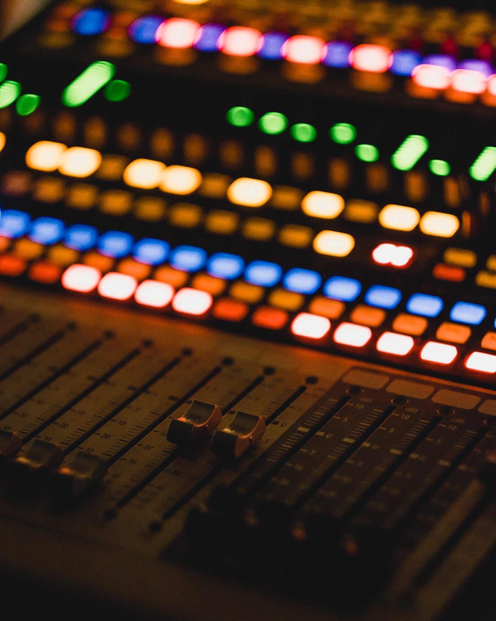 A close-up of an audio mixing console with colourful illuminated buttons and sliders.