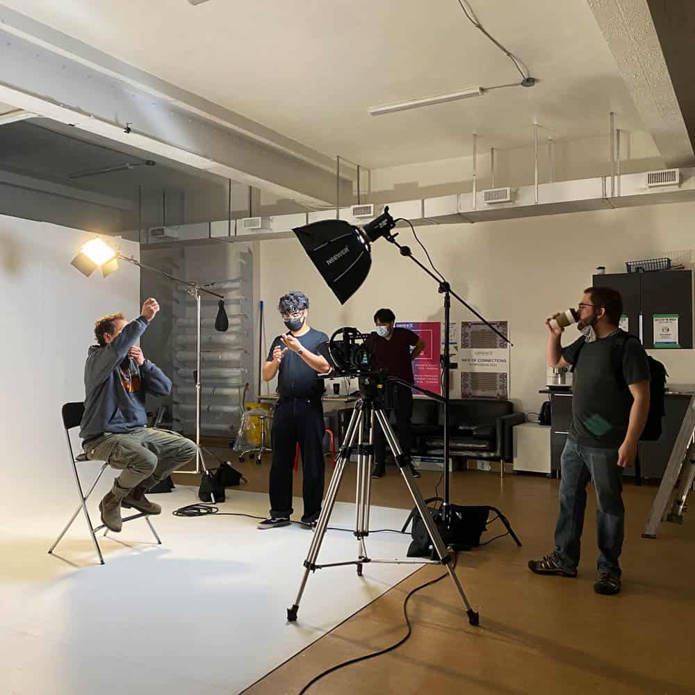 A film crew at work on a set in the Media Arts Studio with a camera and studio lighting.
