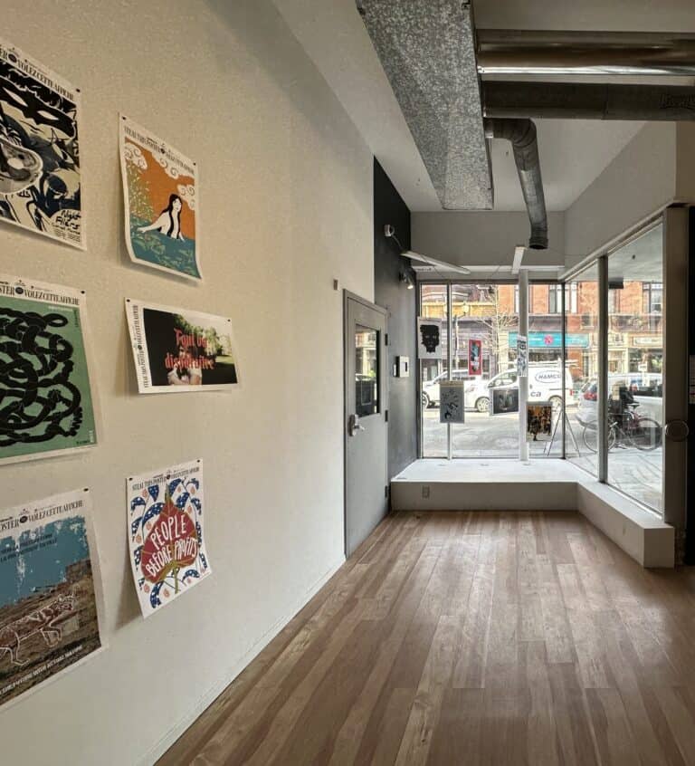 Centre[3]'s Members' Gallery with posters on the left wall, large windows on the right, and a view of the street outside. The space has wooden floors, high ceilings, and visible air ducts.