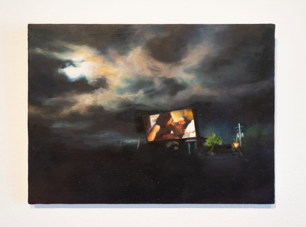 An oil painting of a dark, cloudy night sky with light breaking through the clouds. A drive-in theatre movie screen lights up the centre of the painting, displaying two people in an embrace kissing. The foreground is mostly shadowy, with faint outlines of trees and electric poles.