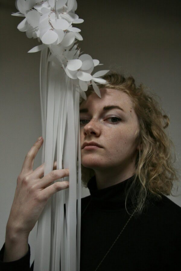 Portrait of Olivia Brouwer holding a sculptural arrangement of white paper-like forms beside their face