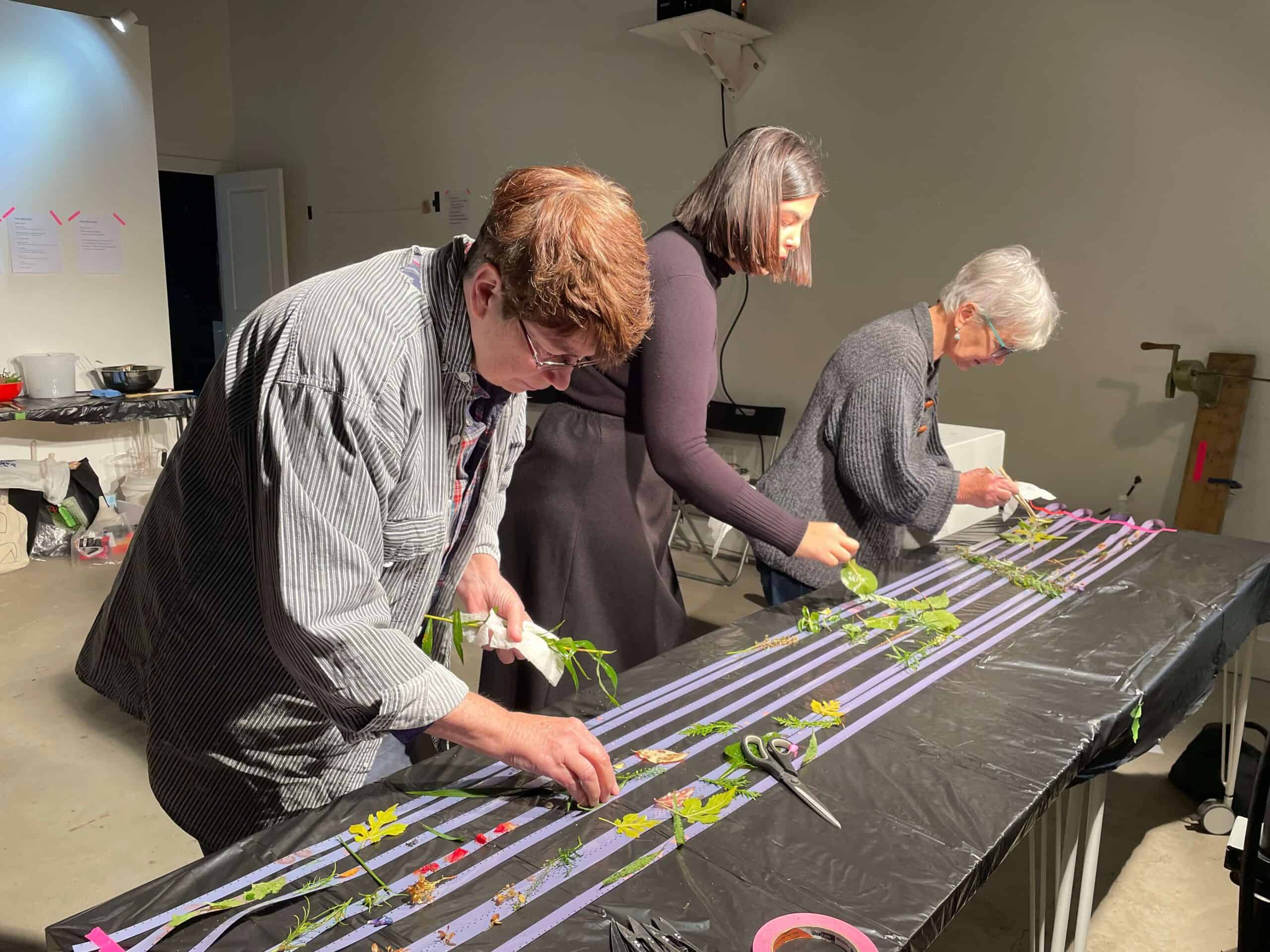 Participants arranging pressed flowers and plant stems at a long workshop table.