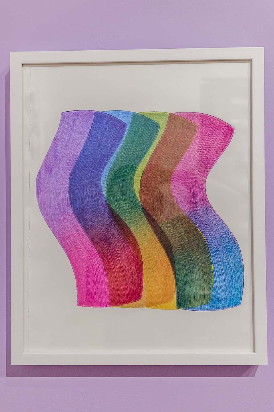 A framed abstract artwork features five wavy, overlapping shapes in gradient colors including pink, purple, blue, green, yellow, and brown, displayed against a lavender wall.