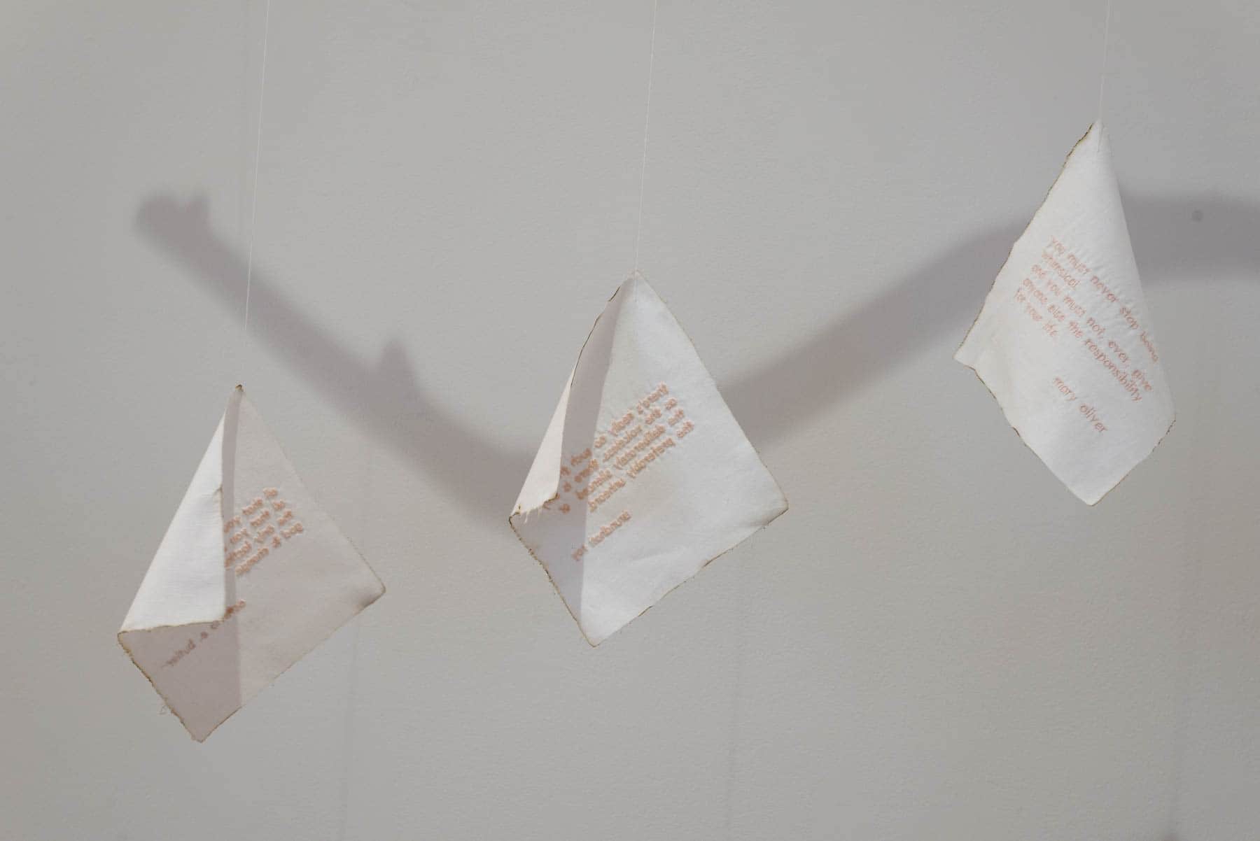 Three suspended paper forms with printed text arranged in a row, casting elongated shadows on a white wall