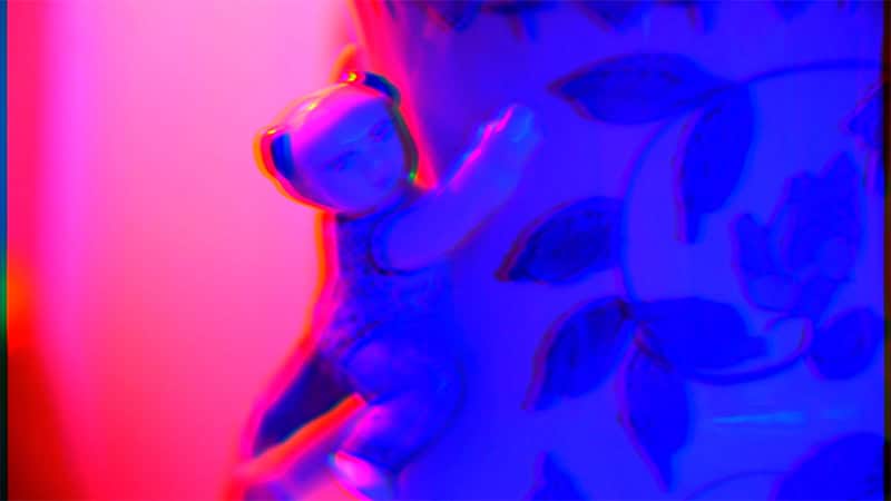 Soft toy figure resting against patterned fabric, shown with strong red and blue colour distortion