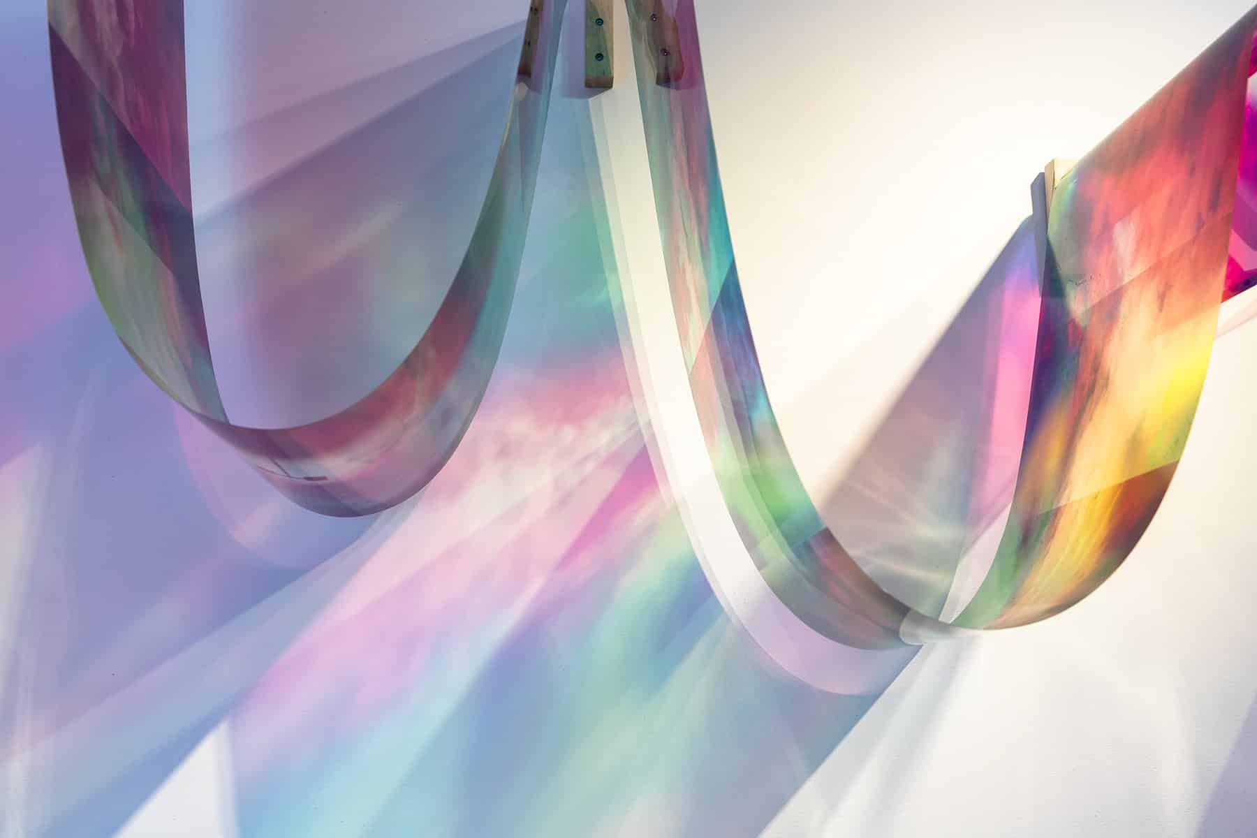 Detail of curved translucent colour panels casting soft rainbow light onto the gallery wall.