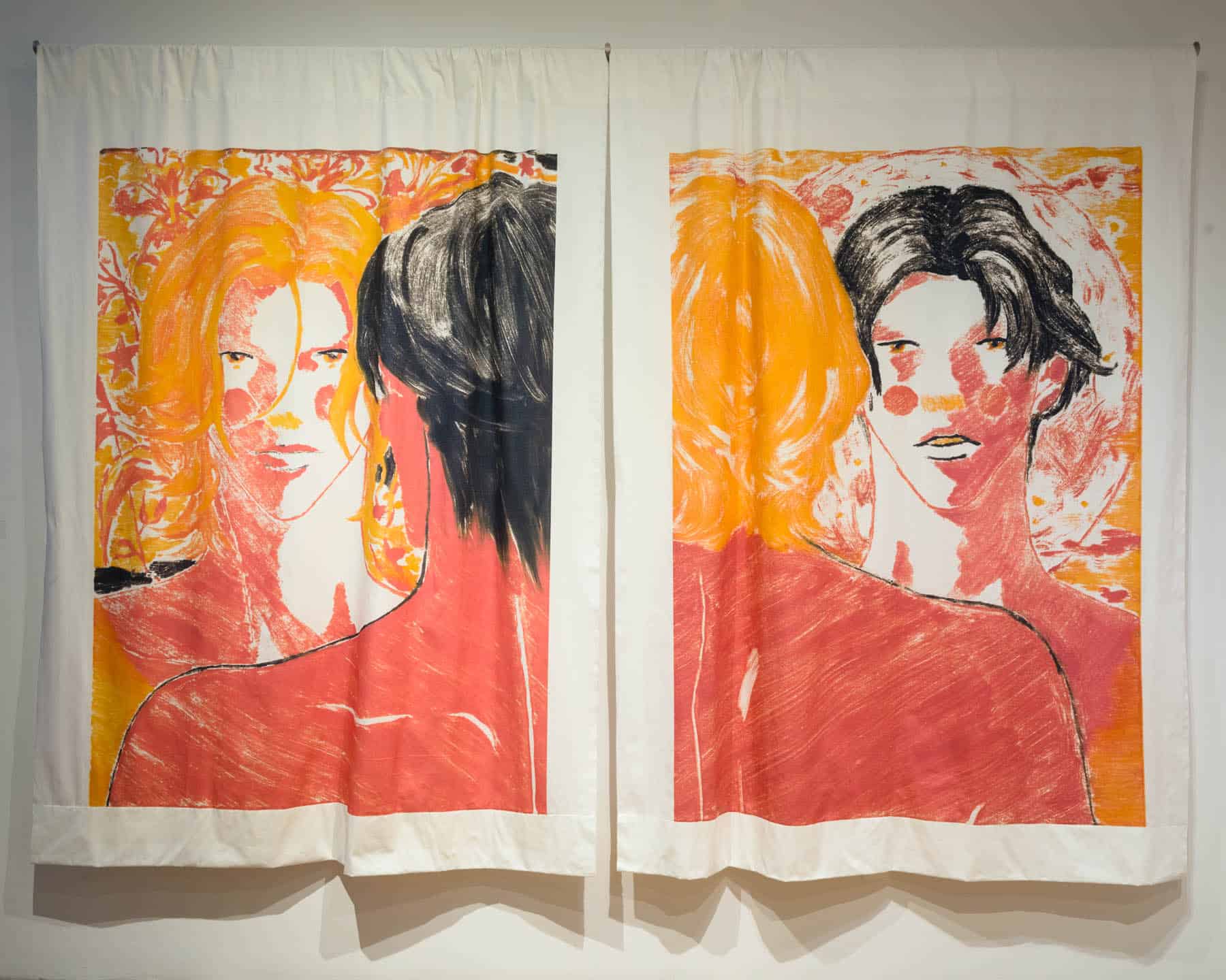 Two large textile panels displaying expressive portraits in red, orange, and black tones hung side by side