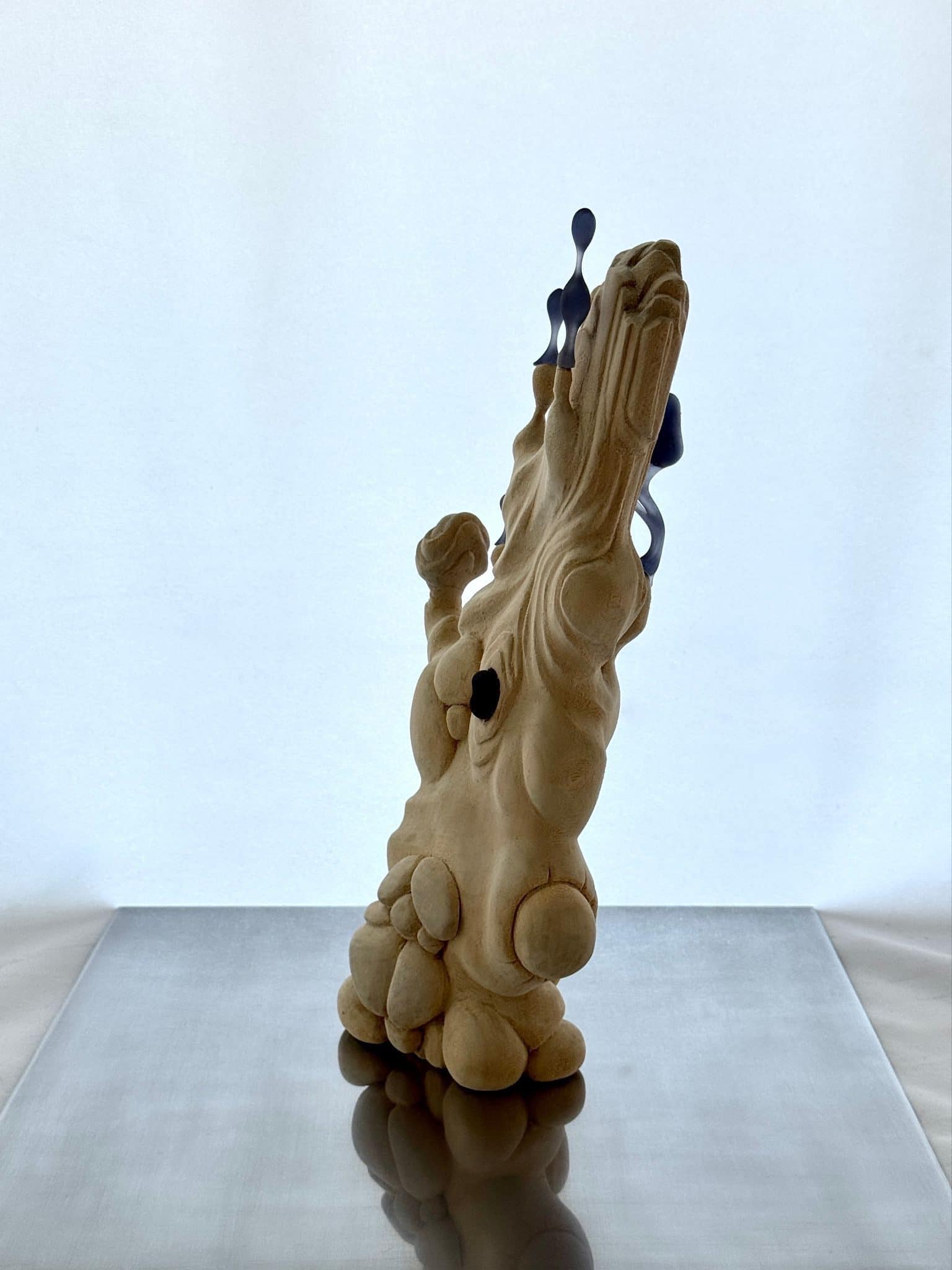 A carved basswood sculpture with dark blue resin inclusions, standing against a pale blue background.
