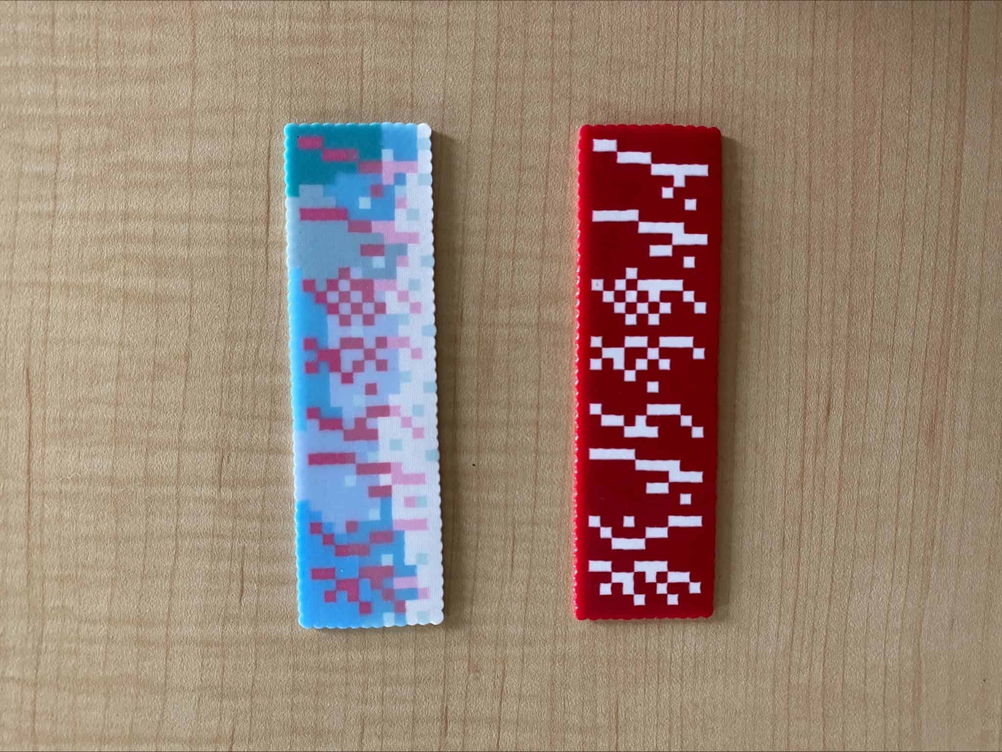 Two narrow perler bead panels on a wooden surface, one blue and white, one red and white, patterned with Nüshu script.